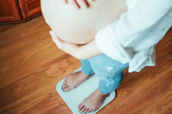 Image of woman weighing herself and experiencing weight gain through pregnancy Coleshill